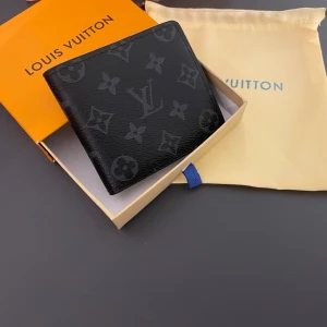 SVART PLÅNBOK  - Snygg svart plånbok  i klassiskt monogrammönster. Tillverkad i läder med flera kortfack och plats för sedlar. Perfekt accessoar för dig som gillar exklusiv och stilren design kommer även med box och dustbag 