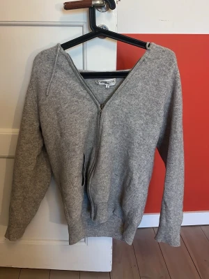Grå cashmerekofta från Davida - Mysig grå kofta från Davida i 100% cashmere. Koftan har dragkedja framtill, långa ärmar och riktigt sköna fickor! Perfekt för dig som gillar stilrena och bekväma plagg.