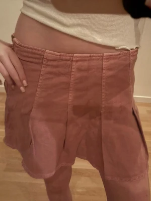 Rosa skort med veckad design - Trendig rosa skort med bred linning och markerade sömmar. Kjoldelen har snygga veck framtill och shortsdelen ger en avslappnad men ändå chic look. Perfekt för dig som vill ha kjolkänsla men ändå känna dig bekväm.