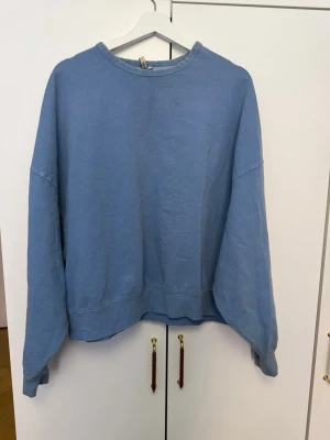 Ljusblå oversized sweatshirt - En enkel och stilren ljusblå sweatshirt med avslappnad passform och rund hals. Tröjan har långa ärmar och ribbade muddar vid ärmslut och nederkant. Perfekt för en chill och casual look. Materialet känns mjukt och bekvämt mot huden.