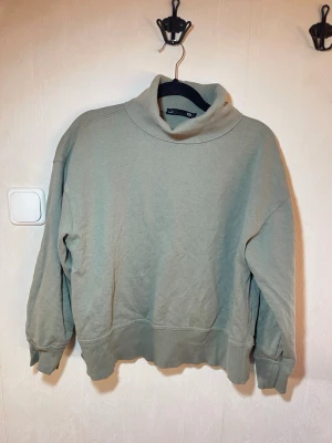 Mintgrön hoodie med hög krage - Mysig mintgrön hoodie med hög krage och avslappnad passform. Tillverkad i mjukt sweatshirtmaterial med ribbade muddar vid ärmslut och nederkant. Perfekt för chill dagar och enkel att matcha med jeans eller mjukisbyxor. Fint skick, inga skavanker. Lager 157, storlek M. Djur, rök och parfymfritt hem.