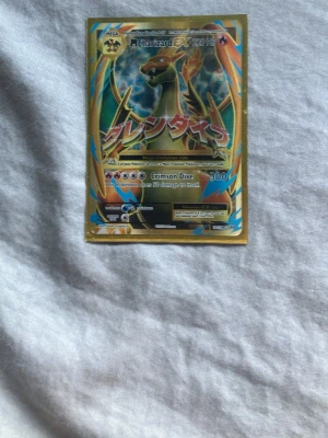 Pokémonkort M Charizard EX - Säljer ett Pokémonkort av typen M Charizard EX med 220 HP. Kortet har en färgstark design med guld, blått och orange och text på både engelska och japanska. Perfekt för samlare eller dig som vill boosta din kortlek.