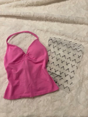 Rosa sportlinne från DFYNE - Snygg rosa sportlinne från DFYNE med halterneck och lätt rynkning vid bysten. Tillverkat i stretchigt material som passar perfekt för träning eller gym. Logga på ryggen och figurnära passform för en sportig look. I modellen impact och färgen blossom🩷🌸 oanvänd