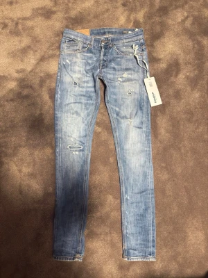 Dondup jeans George  - Säljer ett par ljusblå skinny jeans från dondup  med slitningar och distressed detaljer. Jeansen har klassisk femficksmodell, låg midja och vita sömmar. Materialet är bomull med stretch för extra komfort. Perfekta för en trendig och avslappnad look.