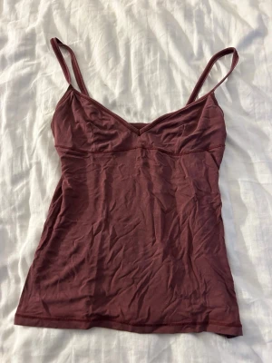Röd linnetopp med smala band - Säljer en enkel och stilren mörkröd linnetopp med smala axelband och v-ringad urringning. Toppen är figurnära och passar perfekt till både jeans och kjol. Materialet känns mjukt och stretchigt.