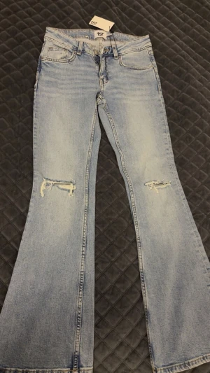 Ljusblå bootcut jeans med hål slitningar - Säljer ett par ljusblå bootcut jeans från lager 157 med hål slitningar på knäna. Byxorna är helt nya, har aldrig använt de. Köpte de för 400kr. Säljer pågrund av att de inte passar mig. Prislappen finns kvar.