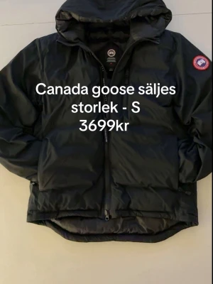 Svart dunjacka från Canada Goose - Säljer en svart dunjacka från Canada Goose med huva och dragkedja framtill. Jackan har två stora fickor och den klassiska Canada Goose-loggan på ärmen. Perfekt för kalla vinterdagar och riktigt varm tack vare dunfyllningen. Kvitto finns 