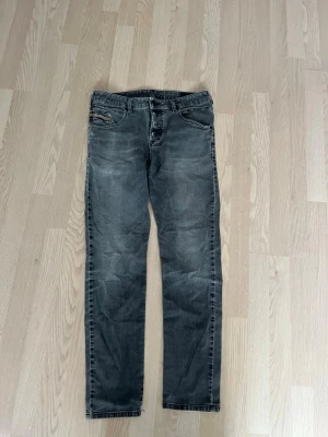 Grå Diesel Jeans - Snygga grå slim fit jeans med knäppning framtill och klassiska fem fickor. Jeansen har en tvättad look och raka ben. Materialet är troligtvis bomull med stretch för extra komfort. 
