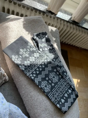 Mörkgrå leggings med vintermönster - Mörkgrå leggings med vita snöflingor, hjärtan och zigzag-mönster. Tjockare material som känns mjukt och stretchigt, perfekt för kalla dagar. Hög midja och elastisk linning för skön passform. Inget synligt märke.