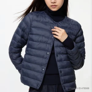 Mörkblå uniqlo jacka  - Stilren mörkblå dunväst med rund halsringning och tryckknappar framtill. Västen har en quiltad design och är lätt vadderad för extra värme. Perfekt att bära över en hoodie eller tröja för en trendig lager-på-lager-look.