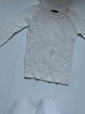 Vit stickad meshtröja Gina Tricot - Vit stickad tröja från Gina Tricot med meshmönstrad framsida och slätstickade ärmar. Tröjan har rund halsringning och ribbade muddar vid ärmslut och nederkant. Perfekt för lager på lager och en cool, avslappnad stil.