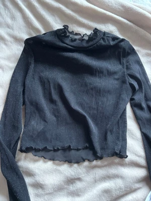 Svart glittrig transparent cropped top - Svart långärmad cropped topp med glittrigt tyg med volanger🤍✨  Genomskinlig och perfekt för festliga outfits – fungerar utmärkt med svart BH under. Croppad modell som sitter tight och framhäver midjan.  Storlek S. Jag är 170 cm och brukar ha storlek S/M – toppen sitter fint på mig.  Nästan aldrig använd, troligtvis från Monki eller Pull&Bear. En perfekt party- eller kvällsoutfit som verkligen lyser på dansgolvet 💫
