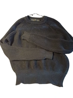 Svart stickad tröja från 157 - Säljer en svart stickad tröja från 157 med grov ribbstickning. Tröjan har rund halsringning, långa ärmar och breda muddar vid ärmslut och nederkant. Perfekt för lager på lager och enkel att matcha med olika outfits.