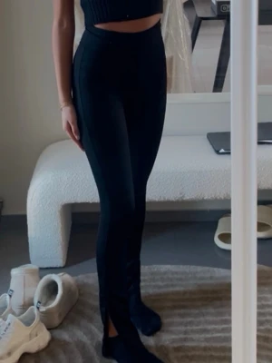 Svarta ribbade leggings med slits - Säljer ett par svarta leggings med hög midja och ribbad struktur. De har en snygg slits vid ankeln framtill som ger en trendig look. Perfekta att matcha med crop tops eller oversized tröjor. Materialet är stretchigt och följsamt för en bekväm passform.