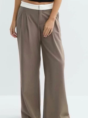 Vida kostymbyxa med kontrastlinning - Snygga vida kostymbyxor i beige med vit kontrastlinning. Byxorna har hög midja, pressveck och lös passform för en trendig siluett. Perfekta för dig som gillar en avslappnad men stilren look.