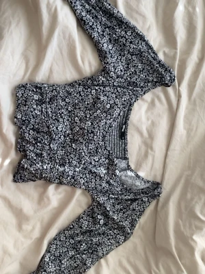 Svart blommig långärmad blus ifrån BikBok - Supersöt svart blus med vita småblommor och lång ärm. Modellen är croppad med lätt volang i nederkant och har en snygg v-ringning. Perfekt att styla med jeans eller kjol för en trendig look.