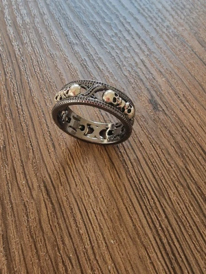 Silverfärgad punkring med döskallar - Snygg silverfärgad punkring med dekorativa döskallar och ett unikt, utskuret mönster runt hela ringen. Ringen har en vintageinspirerad design med små pärlor och fina kanter. Zinklegering. Perfekt för dig som gillar detaljerade accessoarer. Storlek 10.