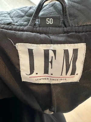 Svart skinnjacka från Jofama - Snygg svart skinnjacka från J.F.M. med stilren design och raka linjer. Jackan har quiltade detaljer på axlarna, två dragkedjeförsedda fickor och en klassisk krage utan slag. Perfekt för dig som gillar en tidlös och cool look.                                                         Köpte denna jacka för 2500kr för ett tag sedan men har växt ur den och  inte använt den på ett tag. Den passar perfekt som vårjacka med en tunn tröja under om man har L. 