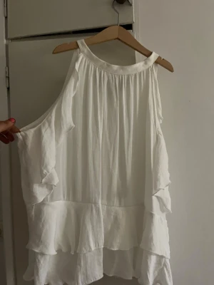 Vit volang topp  - Säljer en luftig vit topp med volangdetaljer. Toppen har en lös passform och är perfekt för varma dagar. Materialet känns lätt och svalt, och volangerna ger en extra touch till looken. Toppen är i storlek L men skulle säga att den passar som m och s också då mina vänner lånat den