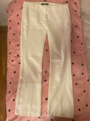 Vita kostymbyxor från BikBok - Skitsnygga vita kostymbyxor från BikBok med raka ben och pressveck. Byxorna har diskreta fickor fram och hällor för skärp i midjan. Perfekta för en clean och stilren look. Materialet känns mjukt och har ett fint fall.