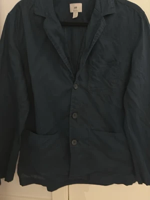 Mörkblå overshirt från H&M Regular Fit - Stilren mörkblå kavaj från H&M i Regular Fit. Kavajen har tre knappar framtill, två stora fickor nedtill och en bröstficka. Tillverkad i ett lätt tyg som ger en avslappnad men ändå dressad look. Perfekt för dig som vill ha en enkel och snygg overshirt storlek S