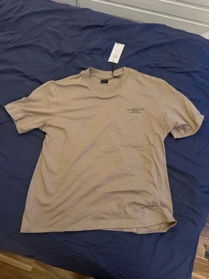 Beige t-shirt från Jack & Jones XL - Snygg beige t-shirt från Jack & Jones Premium i storlek XL. T-shirten har en klassisk passform, rund halsringning och diskret tryck på bröstet. Tillverkad i mjuk bomull som känns skön mot huden. Perfekt för en avslappnad och stilren look.