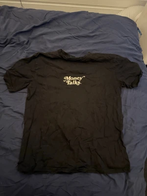 Svart t-shirt FSBN Money Talks - Svart t-shirt från FSBN med texten 'Money Talks' i vitt tryck på bröstet. Modellen är relaxed fit och har klassisk rund hals och korta ärmar. Tillverkad i mjuk bomull som känns skön mot huden.