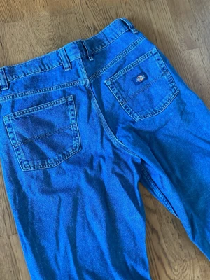 Blå baggy jeans från Dickies - Säljer ett par blå baggy jeans från Dickies med klassisk femficksdesign och bred passform. Jeansen har hällor för skärp och Dickies-logga på ena bakfickan. Perfekta för en avslappnad streetstil.