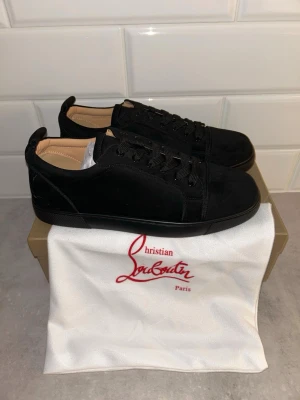 Svarta sneakers Christian Louboutin - Stilrena svarta sneakers Christian Louboutin i mocka med matchande svarta skosnören och diskret design. Låg modell med klassisk siluett och beige innerfoder. Perfekta för dig som gillar exklusiva och minimalistiska skor.