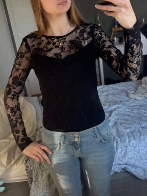 Svart spetsbody med långa ärmar - Snygg svart body med långa ärmar i spets och rund halsringning. Spetsdetaljer över kroppen, axlax och ärmar 