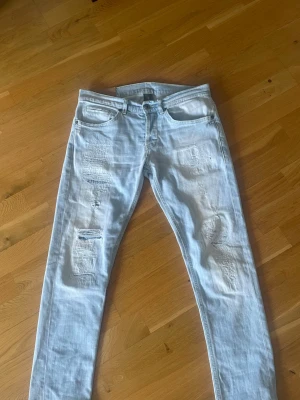 Ljusblå slitna dondups med patchar - Säljer ett par ljusblå dondups med slitningar och patchade detaljer på framsidan. Jeansen har fem fickor, lite mer slimmad passform och en klassisk knappgylf. Snygga kontrastsömmar baktill och en liten logga på linningen. Perfekta för en avslappnad streetstil.