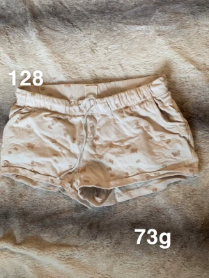 Beige shorts med små mönster - Säljer ett par beige shorts med små diskreta mönster och snörning i midjan. Shortsen har elastisk midja och är perfekta för varma dagar. 🌸 Fint använt skick. Storlek 128