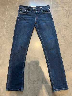 Mörkblå jeans från Replay - Snygga mörkblå jeans från Replay med klassisk femficksdesign och raka ben. Jeansen har kontrastsömmar och logotyp-patch bak i midjan. Tillverkade i mjuk denim med lite stretch för extra komfort.