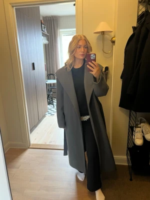 Grå lång kappa med bred krage - Snygg grå kappa med bred krage och knytskärp i midjan. 