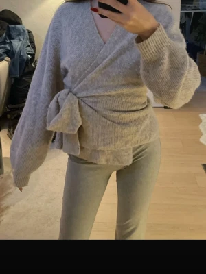 Beige omlottkofta med knytband - Ljusgrå/beige mysig omlottkofta med knytband i midjan. Koftan har en avslappnad passform som ger en trendig look. Perfekt att slänga på sig när det är lite kyligt ute. Materialet känns mjukt och skönt mot huden. Nypris är 990kr!!! Från H&M Bara använd några fåtal gånger! Storlek M men passar mig som har S eftersom man kan knyta lite tajtare:)