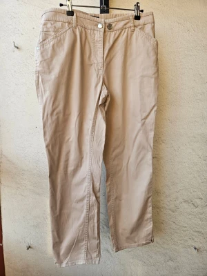 Beige chinos med raka ben - Snygga beige chinos från Franco Callegari med ankellånga, raka ben och klassisk passform. Byxorna har framfickor, bakfickor med knappdetaljer och stängs med knapp och dragkedja. Storlek 40, två knappar för att justera storlek