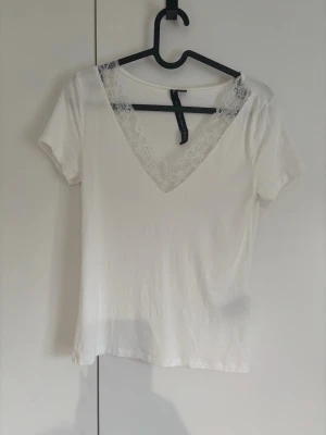 Vit t-shirt med spets från Lager 157🫶🏻 - Snygg vit t-shirt från Noisy May med djup v-ringning och dekorativ spetskant runt halsen. Kortärmad och i mjukt material, perfekt för en trendig och fräsch look. Enkel att matcha med jeans eller kjol. Superfin!🤍