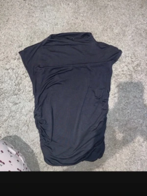 Svart kort topp med rynkade sidor - Snygg svart topp med rynkade detaljer längs sidorna. Toppen  är ärmlös och har en enkel, tight passform som framhäver figuren. Perfekt för dig som gillar stilrena och moderna plagg. Materialet känns mjukt och stretchigt.