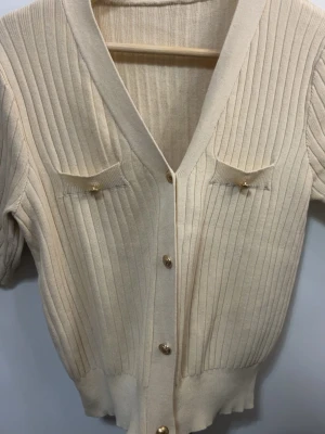 Beige ribbstickad kofta med guldknappar - …