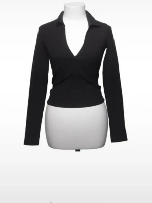 Svart långärmad - Stilren svart långärmad topp med djup v-ringning och klassisk krage. Toppen har en slim passform och är perfekt för att skapa en clean och trendig look. Materialet är stretchigt och bekvämt, vilket gör den enkel att bära hela dagen.