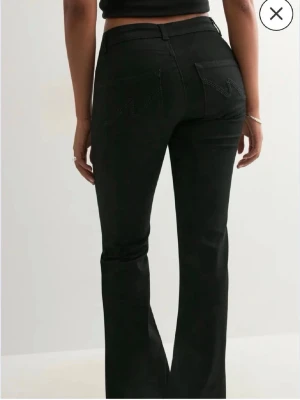 Svarta bootcut jeans från Nelly  - Säljer ett par svarta bootcut jeans från Nelly med klassisk femficksdesign och broderad detalj på bakfickorna. Jeansen har låg midja och utsvängda ben, perfekta till sneakers eller boots. Materialet är stretchigt denim för extra komfort.