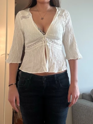 Vit blus med söta detaljer - Säljer en vit blus i boho-stil med trekvartsärmar och v-ringning från ZARA. Blusen har dekorativa spetsdetaljer och knappar framtill. Den är även öppen framtill. Nästan aldrig använd. Säljer pga att den är för stor vid brösten. 