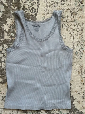 Ljusblått brandy linne - Säljer en ljusblå ribbad linnetopp från Brandy Melville med fina spetsdetaljer runt halsringning och ärmhål. Toppen är ärmlös och har en enkel, slim passform som är perfekt för att matcha med jeans eller kjol. Onesize men sitter som S