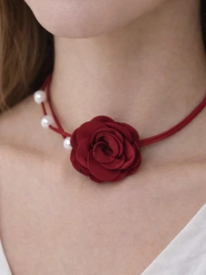 Choker med röd ros och pärlor - Chokerhalsband med en stor röd tygros i mitten och vita pärlor på ena sidan. Bandet är tunt och rött, vilket ger en romantisk och trendig look. Perfekt för att lyfta vilken outfit som helst med en unik detalj.