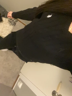 Svart stickad tröja Polo Ralph Lauren - Klassisk svart stickad tröja från Polo Ralph Lauren med vit broderad logga på bröstet. Tröjan har rund halsringning och ribbade muddar vid ärmslut och nederkant. Perfekt för en stilren och enkel look.