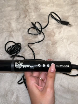 Locktång Remington svart med väska - Säljer en svart locktång från Remington med silvriga detaljer och blommönster. Kommer med en matchande silvrig värmeskyddande väska. Locktången har tre knappar för inställningar och lång sladd för smidig användning. Aldrig använt.