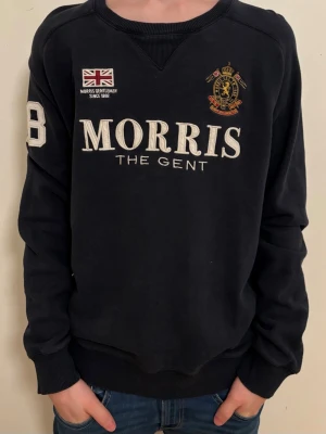 Mörkblå tröja från Morris - Säljer en stilren mörkblå tröja från Morris med tryck på bröstet och en Union Jack-flagga.  Använd kanske 4-5 gånger, köpte den för 1300kr, det finns ett litet hål i den men det syns knappt.