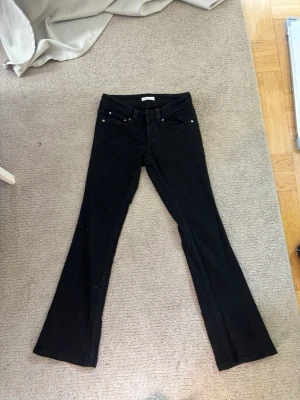 Svarta bootcut jeans från Gina Tricot - Säljer ett par svarta bootcut jeans från Gina Tricot med klassisk femficksdesign och snygga ficklock bak med silverknappar. Jeansen har utsvängda ben och är tillverkade i stretchigt denimtyg för en bekväm passform.