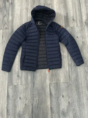 Mörkblå pufferjacka från Save the duck - Mörkblå pufferjacka från Save The Duck. Riktigt skön och snygg javka som går att använde året om skulle jag säga. Den är lite för liten för mig och jag är 180cm. Det är slitage på ena ärmen i fram därav det billiga priset. Annars bra skick, hör av er vid frågor🙌