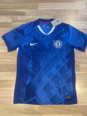 Chelsea FC matchtröja Nike blå - Chelsea FC matchtröja i blått med Palmer och nummer 10 på ryggen. Tröjan har vit Nike-logga och Chelsea-märke på bröstet, samt vita och röda detaljer på sidorna. Tillverkad i lätt och ventilerande material, perfekt för fotbollsträning eller match.